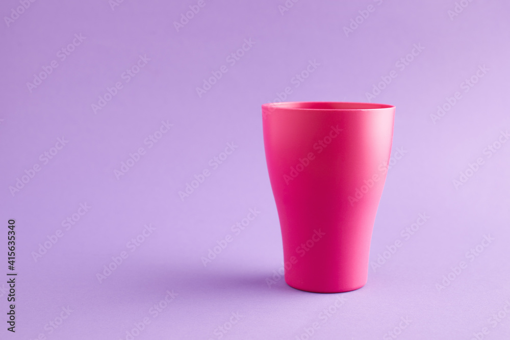 Pink plastic cup at purple background with copy space.
Pink plastic cup at purple background with copy space.