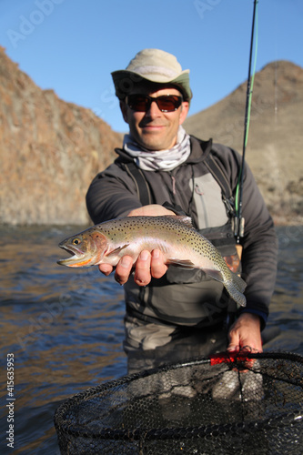 Fotografie happy adult fly fisherman holding a cutthroat trout on a large river with net an