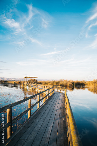 Long wooden bridge surrounded by water and reeds in the 'El Hondo' natural park at sunset. Elche, Alicante, Spain. Vertical. © Gloria