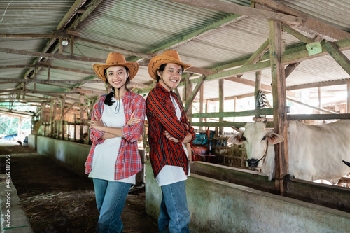 Fototapeta Naklejka Na Ścianę i Meble -  a smiling boy and girl wearing a hat stand back to back in a crossed hands pose in a cow farm stable
