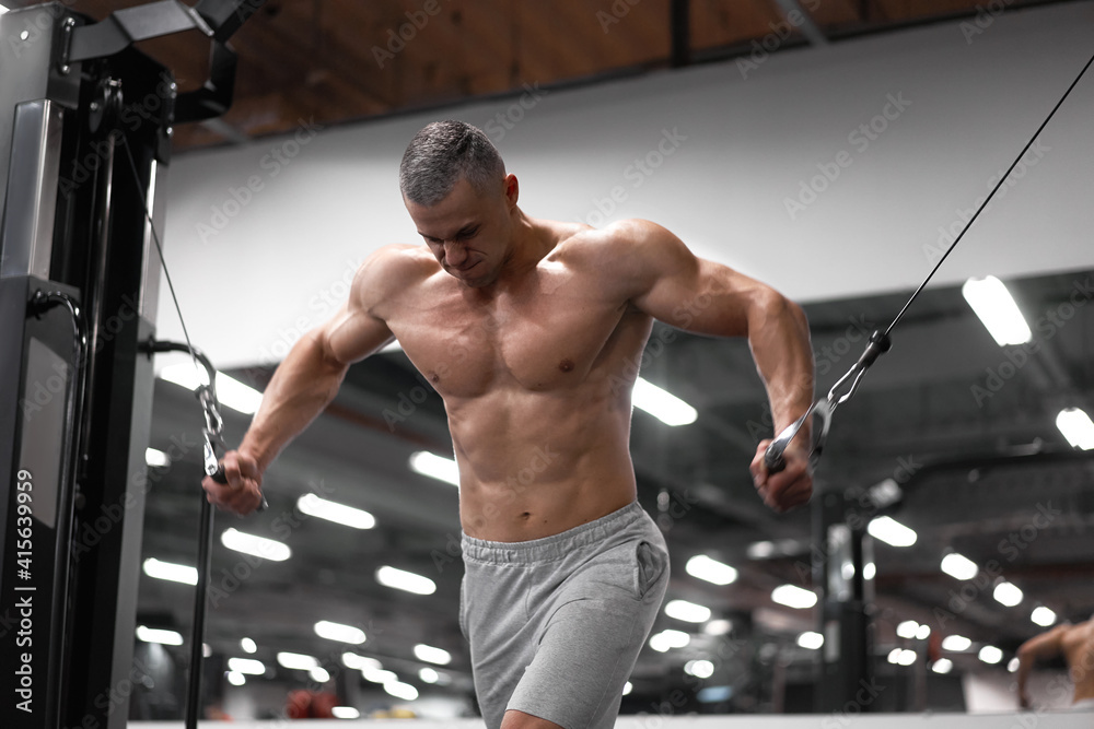 Naklejka premium Muscular athletic bodybuilder standing training chest and shoulders muscles on fitness equipment