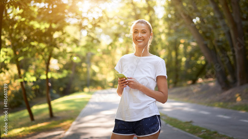 Woman putting on earphones to listen music before jogging summer park