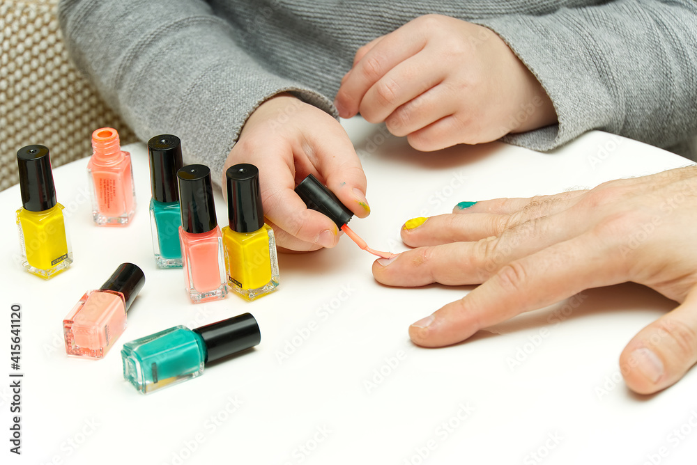 Girl paints her dad's nails with various colors. LGBT family concept Girl paints her dad's nails with various colors. LGBT family concept