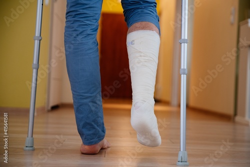 Young man with a broken ankle with a white cast on his leg following a accident. He walking on crutches.