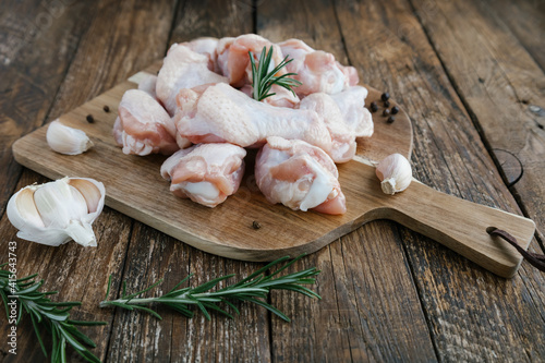 Raw buffalo of chicken wings on cutting board with ingredients for cooking on wooden background. Fresh uncooked drumette or drumstick with garlic, pepper and rosemary. Raw meat. Selective focus.