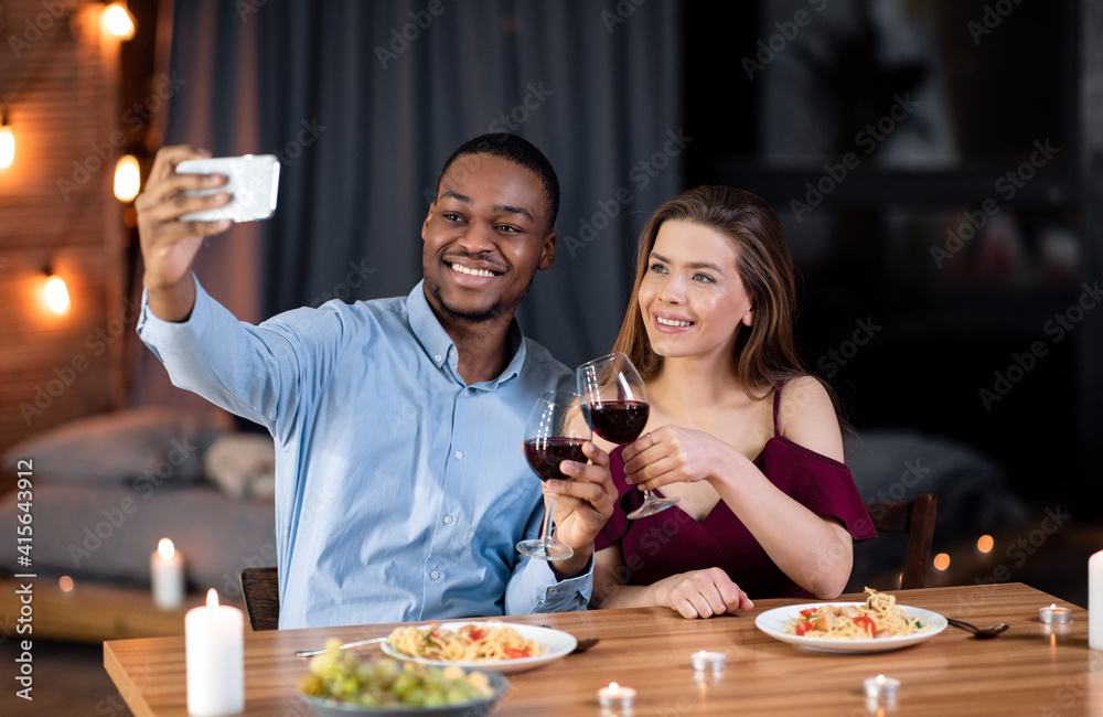 Home Date. Happy interracial couple having dinner and taking selfie on smartphone