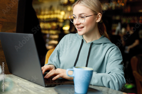 Concentrated at work. Confident young woman in smart casual clothes and glasses, working on laptop. Beautiful smiling female in cafe drink coffee.