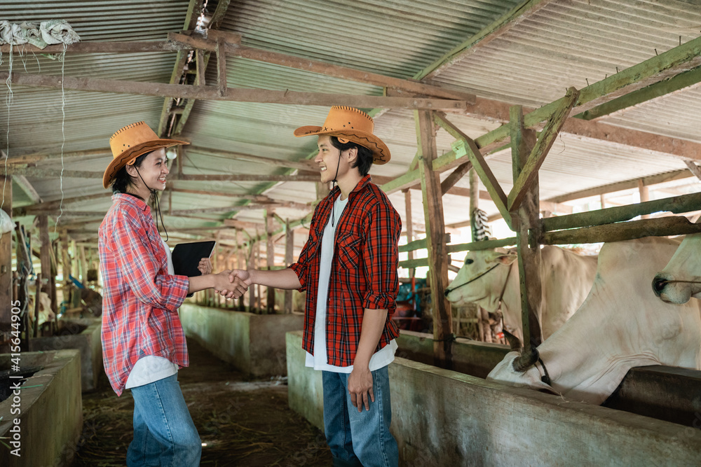 man wearing a hat shaking hands with a cow cattle business partner who carries a digital tablet in the cattle pen