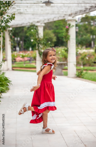 happy little girl in red dress posing in the park outdoors