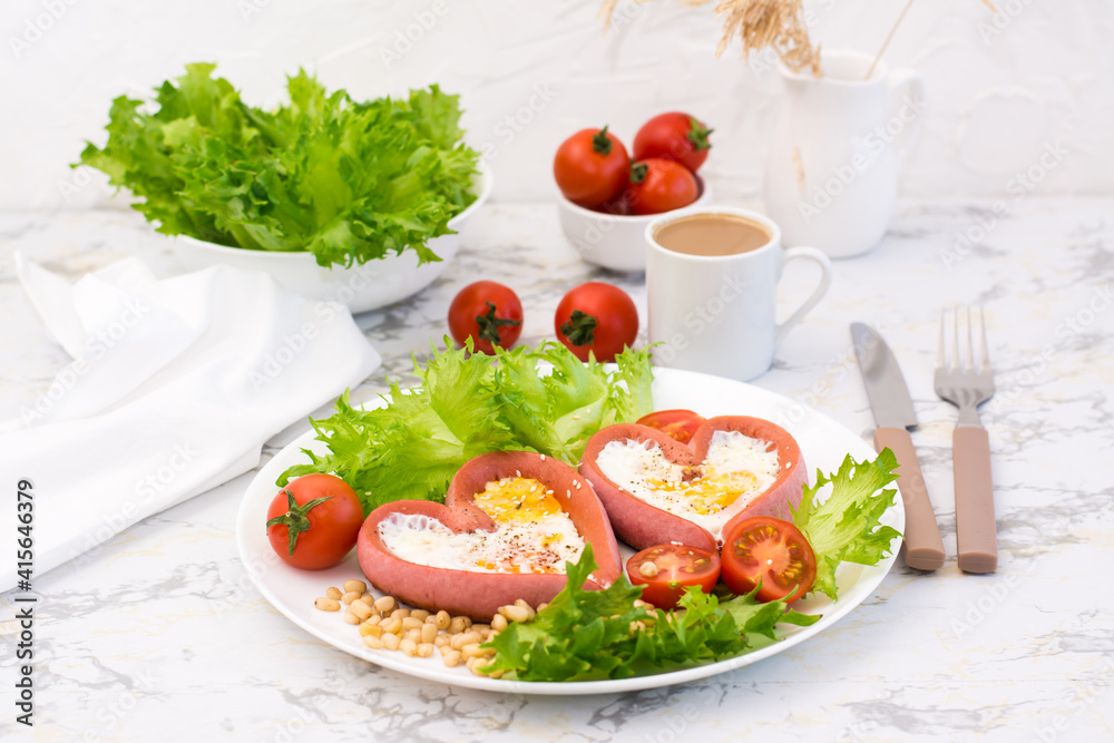 Romantic breakfast. Fried eggs in heart shaped sausages, lettuce and cherry tomatoes on a plate on the table Romantic breakfast. Fried eggs in heart shaped sausages, lettuce and cherry tomatoes on a plate on the table