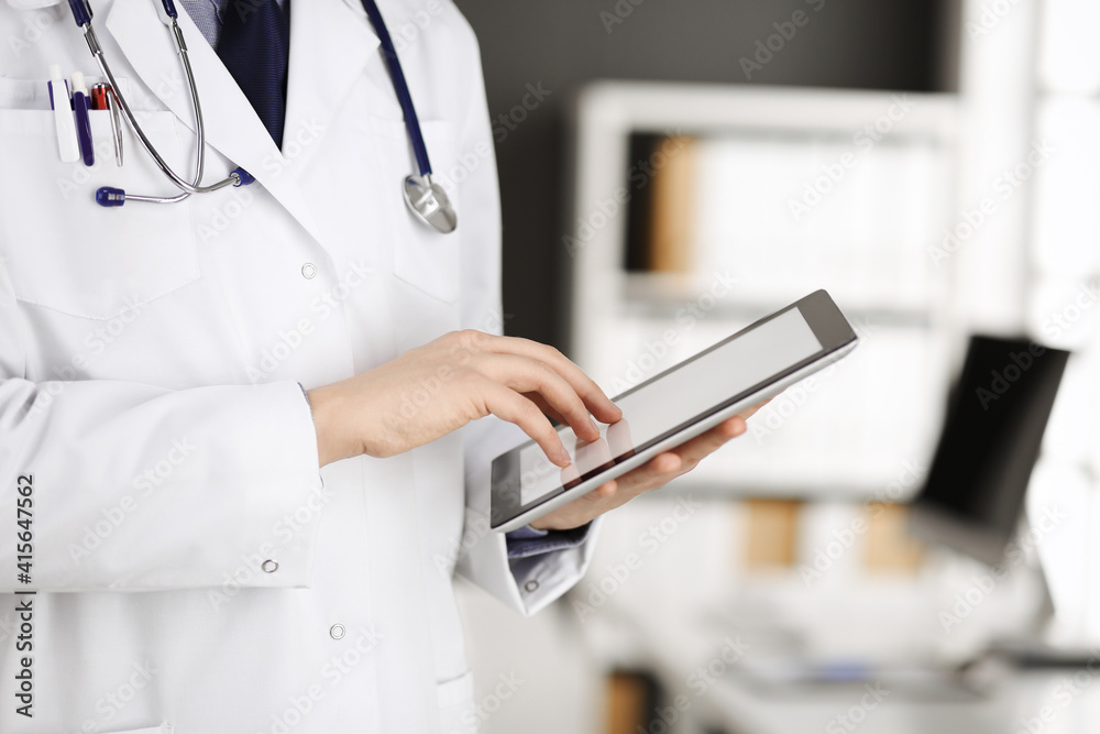Unknown male doctor using tablet computer in clinic near his working place, closeup. Perfect medical service in hospital. Medicine and healthcare concept Unknown male doctor using tablet computer in clinic near his working place, closeup. Perfect medical service in hospital. Medicine and healthcare concept
