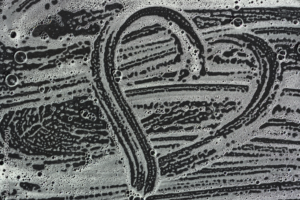Fototapeta premium Background of a dark plate on which soapy water is blurred and bubbles. The foam forms a heart