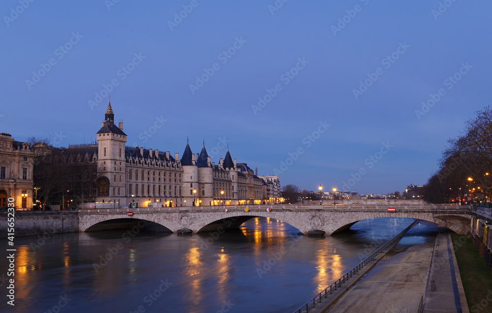 View of Paris by night with a bridge over the Seine river and the Conciergerie building.