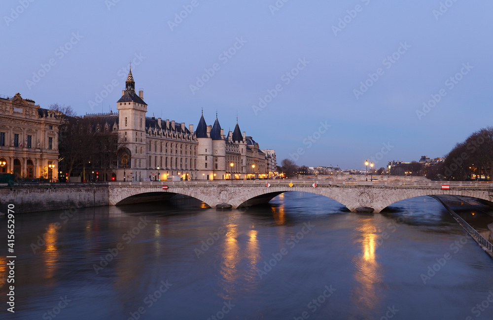 View of Paris by night with a bridge over the Seine river and the Conciergerie building.