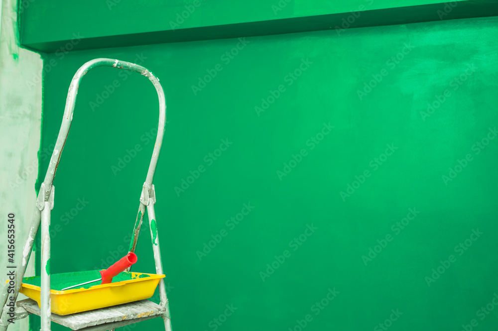 Stepladder, paint tray and roller on the background of a green wall