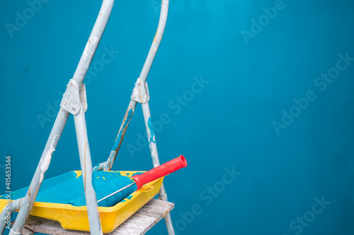 Stepladder, paint tray and roller on the background of a blue wall