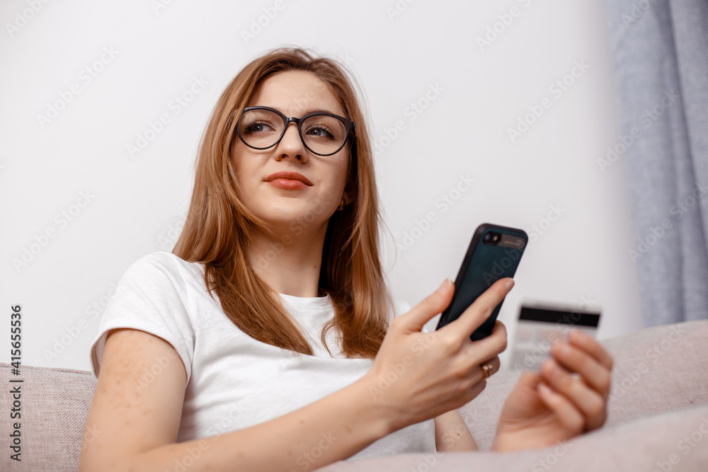 Using smartphone and credit card online shopping. Woman using mobile phone app playing game, shopping online, ordering delivery relax on sofa. A Woman shopping Online On Smartphone With A Debit Card. Using smartphone and credit card online shopping. Woman using mobile phone app playing game, shopping online, ordering delivery relax on sofa. A Woman shopping Online On Smartphone With A Debit Card.