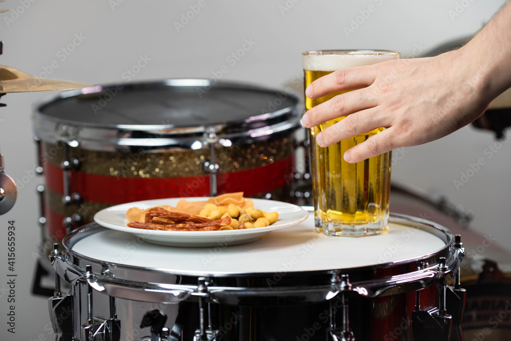Fototapeta premium Glass of light beer with salty snacks on professional drum set closeup. Drumsticks, drums and cymbals, at live music rock concert, in the club stage, bar, or in recording studio
