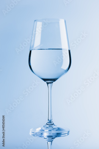 Wine glass. Blue background. Half filled with clear lilquid.