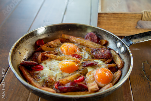 Delicious brunch made of eggs,potatoes,red tomatoes and sausages, served in a pan.