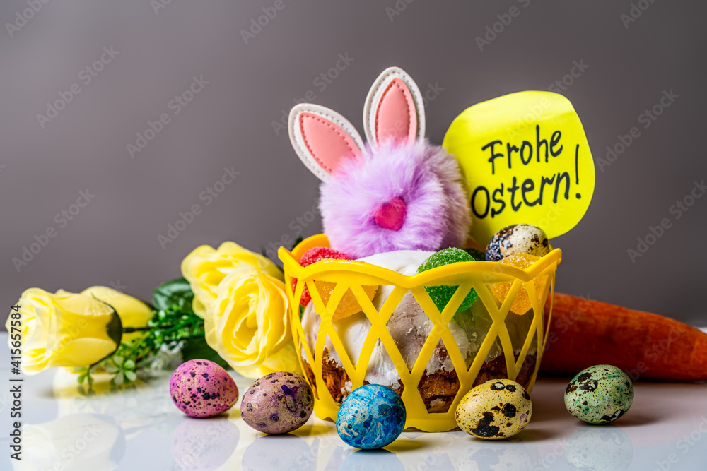 Inscription in German Happy Easter. toy fluffy easter bunny sitting next to carrots, easter eggs and bouquet of flowers