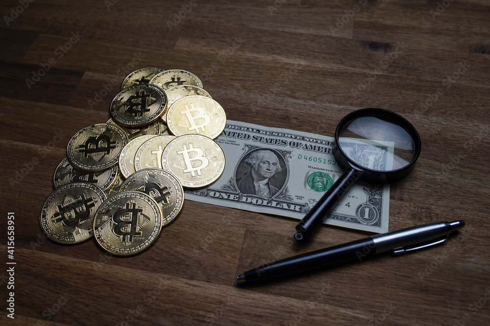 Pile of american dollars cash on brown wooden table. Next to it are several gold bitcoin digital cryptocurrency coins, a pen and a magnifying glass. Bank image and photo background. Pile of american dollars cash on brown wooden table. Next to it are several gold bitcoin digital cryptocurrency coins, a pen and a magnifying glass. Bank image and photo background.