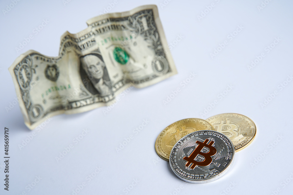 Crumpled american dollars cash on white table. Next to it are several gold bitcoins and a silver digital cryptocurrency coin. Bank image and photo background.