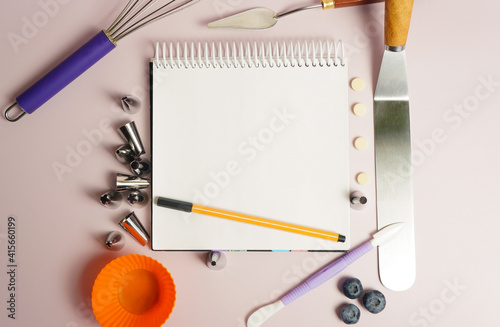 tools for creating and decorating a cake, various spatulas and cream nozzles with an open notebook and a pen for text and recipes, on a purple background photo