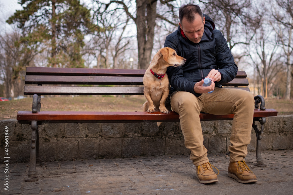 Man reading label on bottle while sitting at the park with his dog