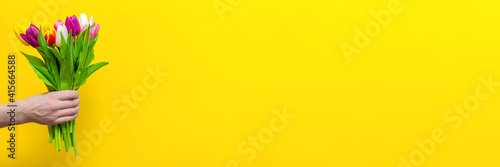 Obraz na plátně A bouquet of flowers in a man's hand on a yellow background