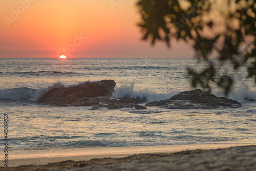 Wave crashing on a rock during the sunset seen from the beach