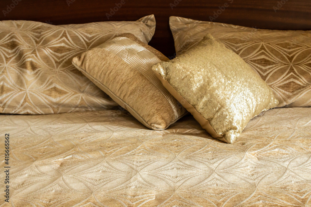 Two gold square throw pillows shining in the sun, sitting on a matching gold patterned duvet in an Ontario, Canada, bedroom. Two gold square throw pillows shining in the sun, sitting on a matching gold patterned duvet in an Ontario, Canada, bedroom.