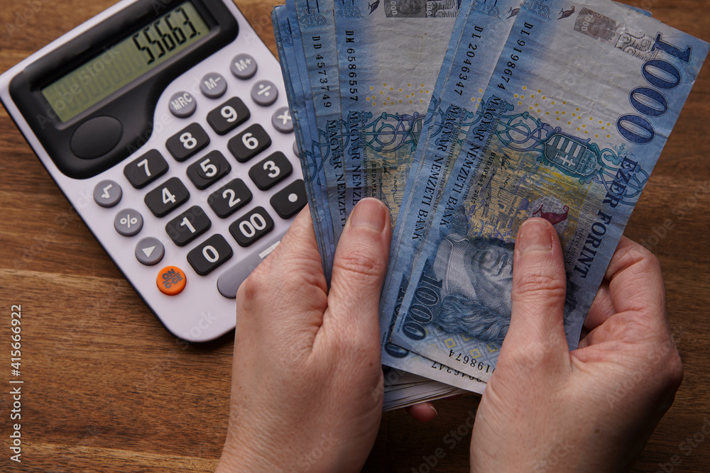 Woman hand holding cash Hungarian forint banknotes, business calculations and expenses, business and people concept. Female hand holding money. The calculator on the wooden table. Woman hand holding cash Hungarian forint banknotes, business calculations and expenses, business and people concept. Female hand holding money. The calculator on the wooden table.