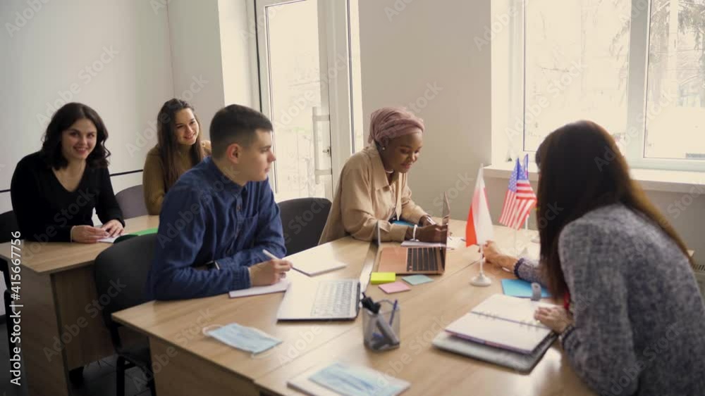 Multiethnic students and teacher study foreign languages together in class. Studing with laptop and medical mask. Black handsome girl student study with white people together
