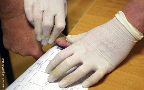 A police officer wearing rubber gloves takes a fingerprint of a suspect.