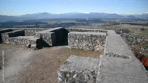 Smlednik castle defensive walls on sunny day in Slovenia. Ruins of renovated castle on hilltop. European and Slovenia flag sway in breeze. Wide angle, left pan photo