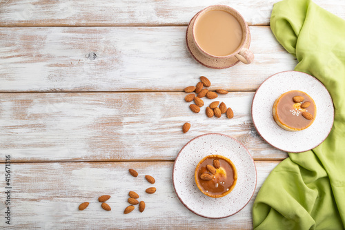 Sweet tartlets with almonds and caramel cream with cup of coffee on a white wooden background. flat lay, copy space.