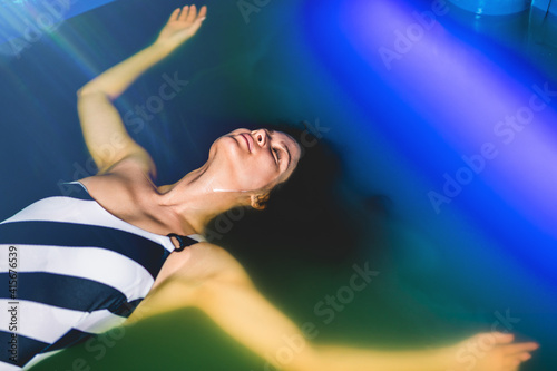 Beautiful woman floating in tank filled with dense salt water used in meditation, therapy, and alternative medicine. .