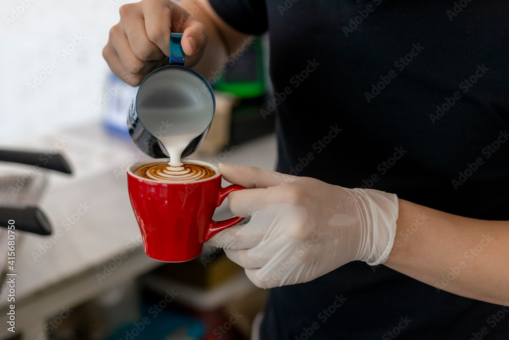 Close up barista pouring steamed milk into coffee cup making beautiful latte, cappuccino art Rosetta pattern. Close up barista hands pouring warm milk in red coffee cup for making latte art.