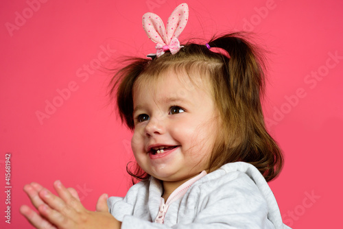 Easter bunny smiling child with rabbit ears and pigtails isolated on pink background. Happy holiday baby toddler.