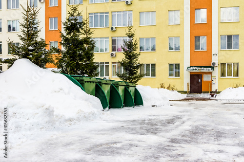 green plastic dumpsters stand between snowdrifts and Christmas trees in the courtyard of an apartment building © Dmitrii