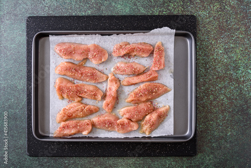 Fresh raw chicken breast cut into chicken strips, on a baking tray with for olive oil and rubbing spices
