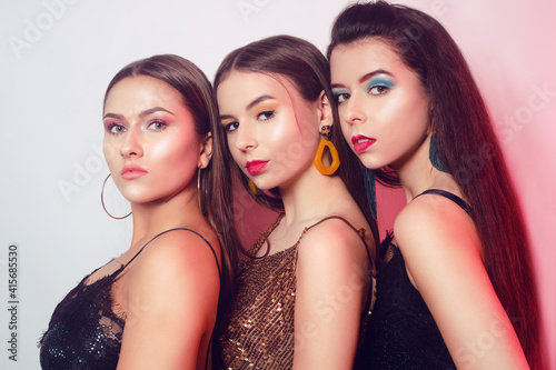 Portraits of three beautiful brunettes on a white background, the girls celebrate March 8, Women's Day. Makeup, accessories and glitter outfits on beautiful women