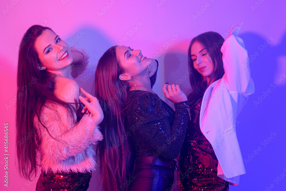 Three beautiful girls are dancing in neon. An incredibly fun party with girls in shiny dresses, celebrate holiday women's day, 8 march, smile, laugh, dance, sing. Night club. Three beautiful girls are dancing in neon. An incredibly fun party with girls in shiny dresses, celebrate holiday women's day, 8 march, smile, laugh, dance, sing. Night club.