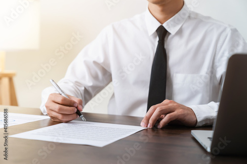 Businessman holds pen and signs agreement contract on the table.