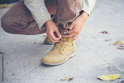 Man kneel down and tie shoes industry boots for worker. Close up shot of man hands tied shoestring for his construction brown boots. Close up man hands tie up shoes for footwear concept.