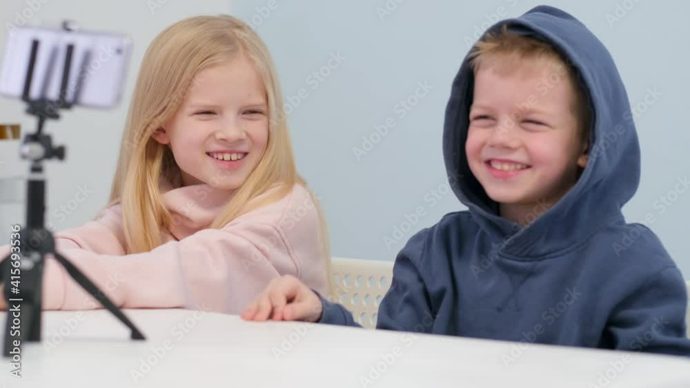 Kids bloggers talking with followers, live streaming looking to smartphone screen at home. Little boy and girl making selfie Kids bloggers talking with followers, live streaming looking to smartphone screen at home. Little boy and girl making selfie