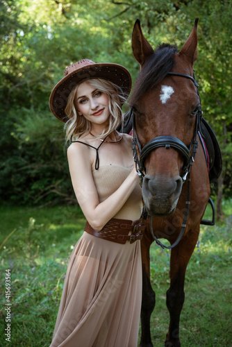 Beautiful young woman in a cowboy hat near a horse on nature in the park