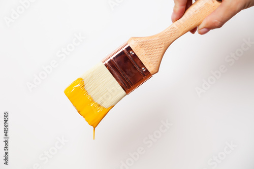 Hand with paintbrush with yellow paint drips off the brush photo