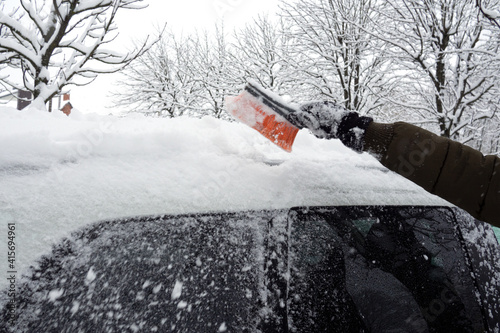 Removing snow from car with a brush. Man cleans his car after a snowstorm.